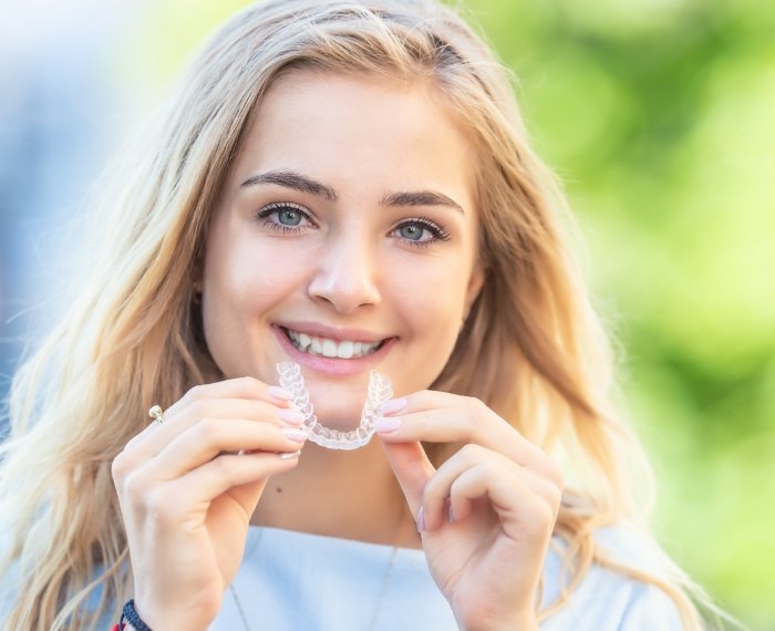 Smiling blonde woman holding an Invisalign aligner