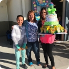 Three people standing on sidewalk holding a multitiered cake