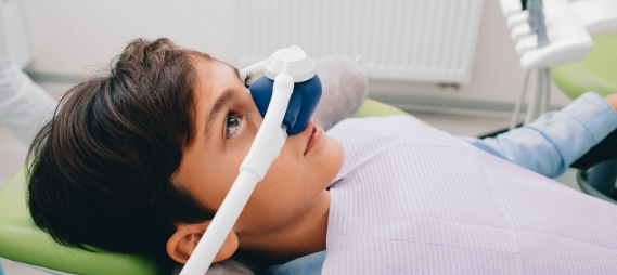 Young boy in dental chair wearing nitrous oxide mask on his nose