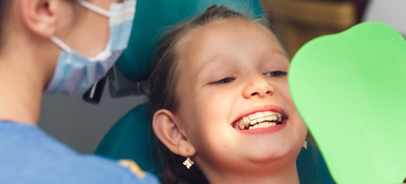 Girl with braces smiling and putting her hand over her face