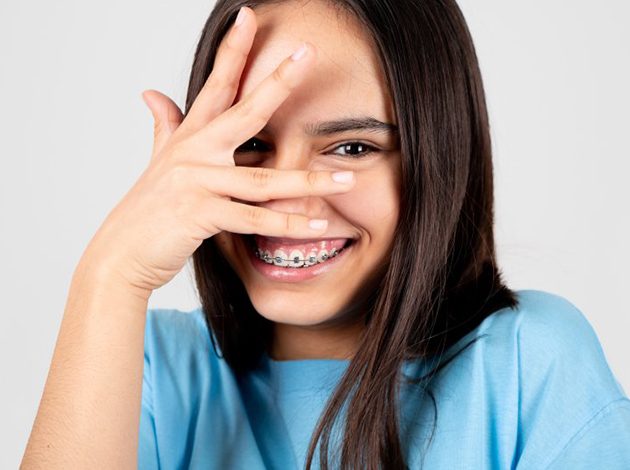Girl with braces in patient’s chair smiling in handheld mirror